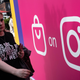 A woman wearing a black t shirt walks by a wall sporting a shopping bag symbol and the Instagram logo.